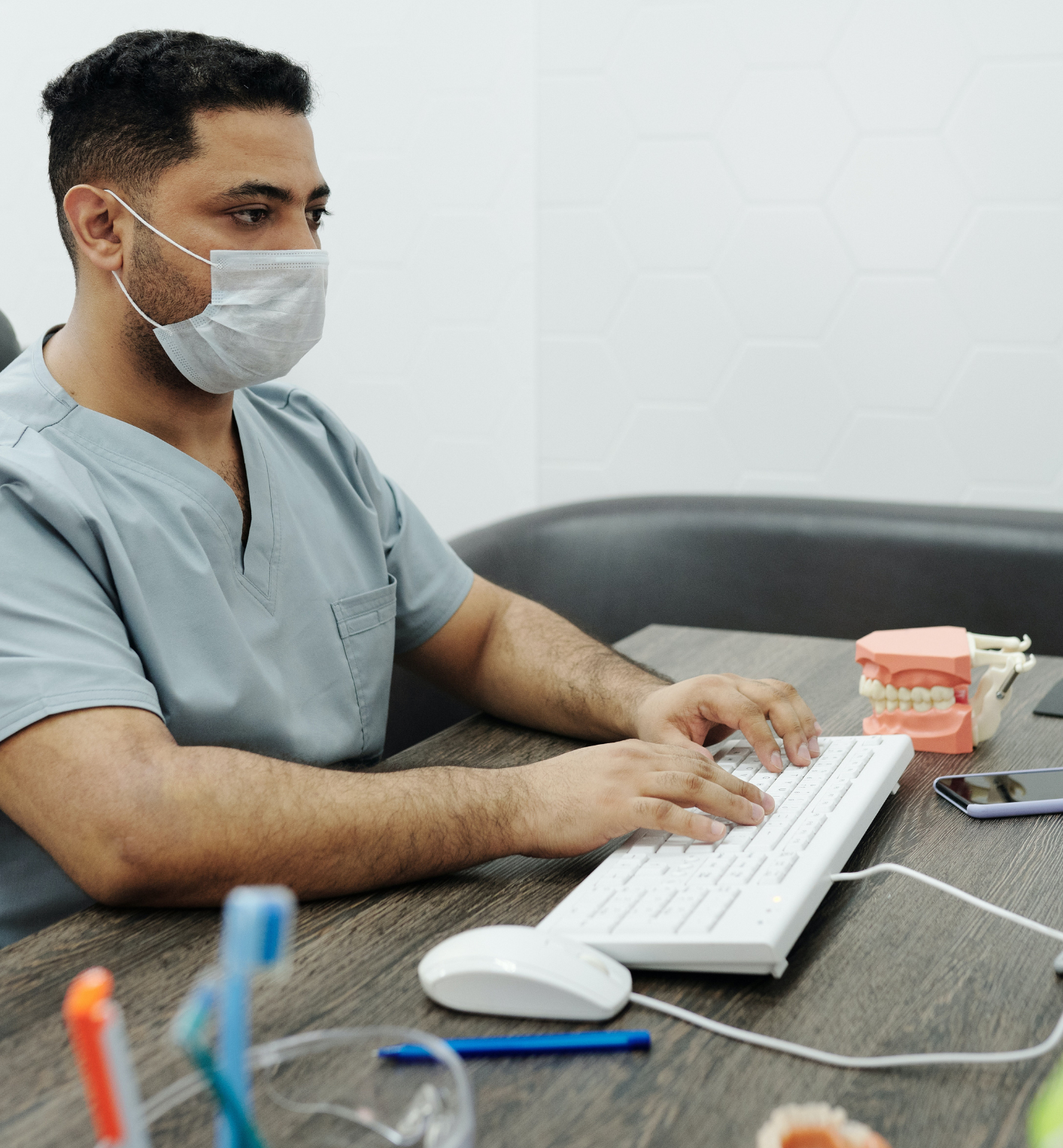 Dentist in facemask sitting down at desk typing on a computer