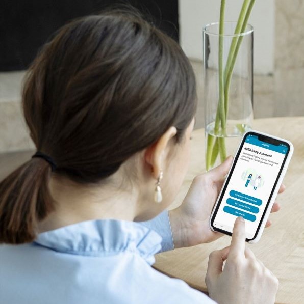 Woman with dark hair in low ponytail. Back is to the camera. She is looking at the welcome screen of the DigiBite teledentistry mobile app